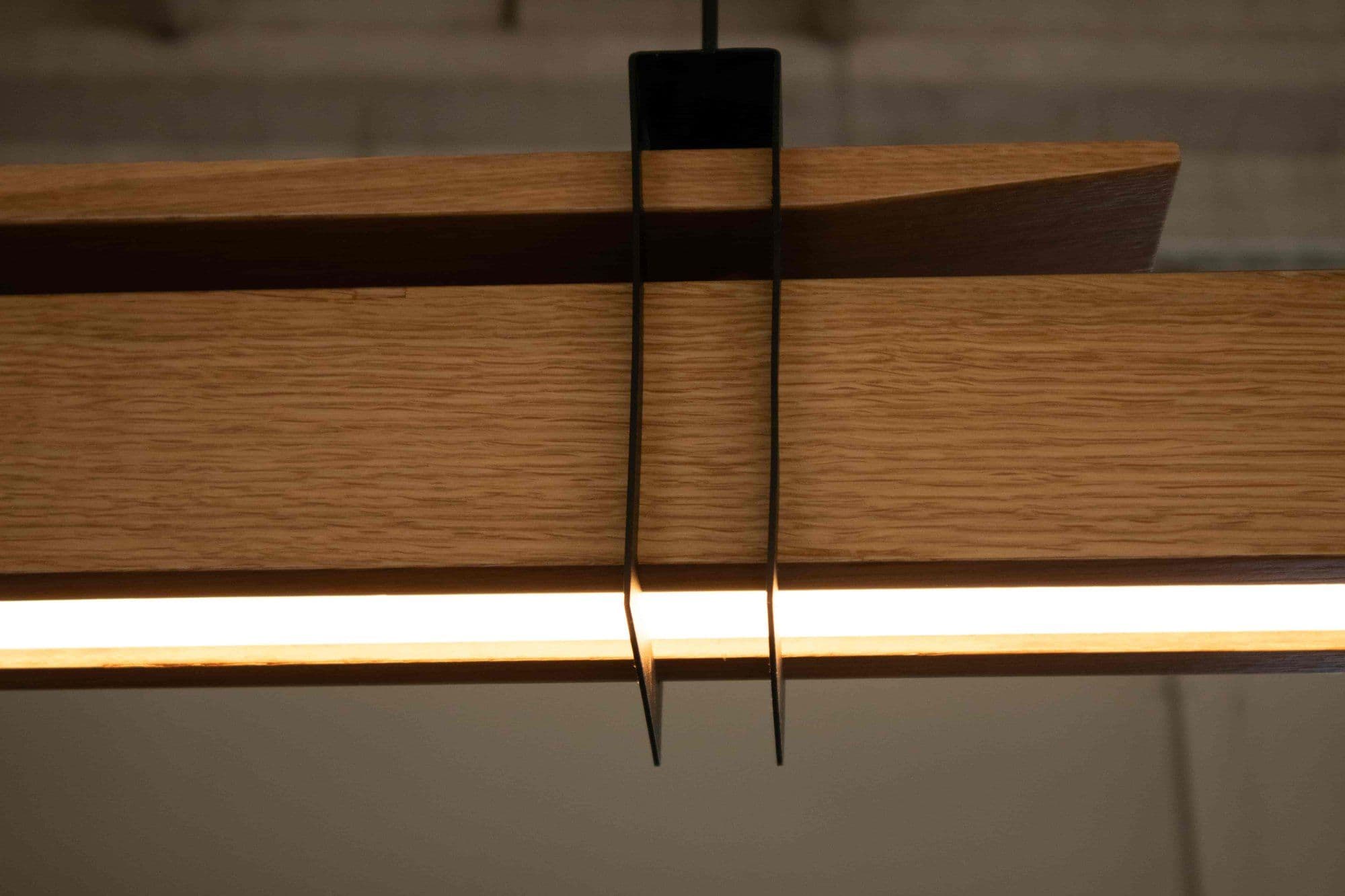 Detalle de la madera de la lámpara colgante Kanna con la luz cálida que corre por debajo de la barra