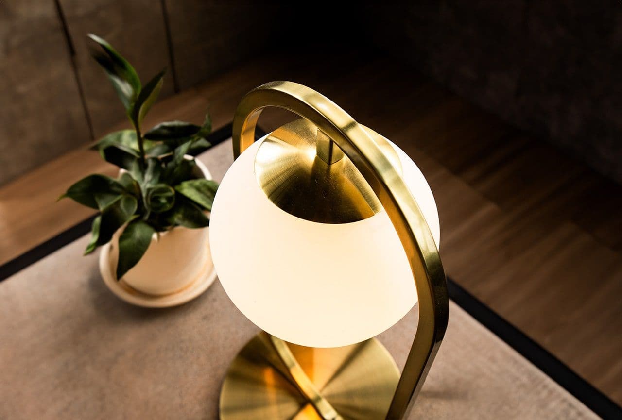 Velador Bubble con globo de cristal blanco y arco metálico dorado, encendido junto a una planta